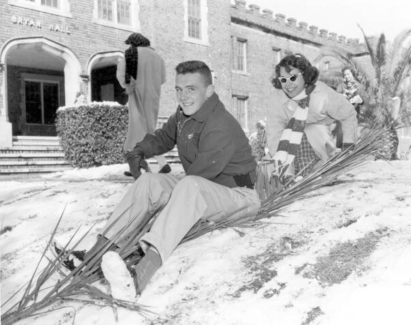 A man and woman are sitting in the snow trying to sled