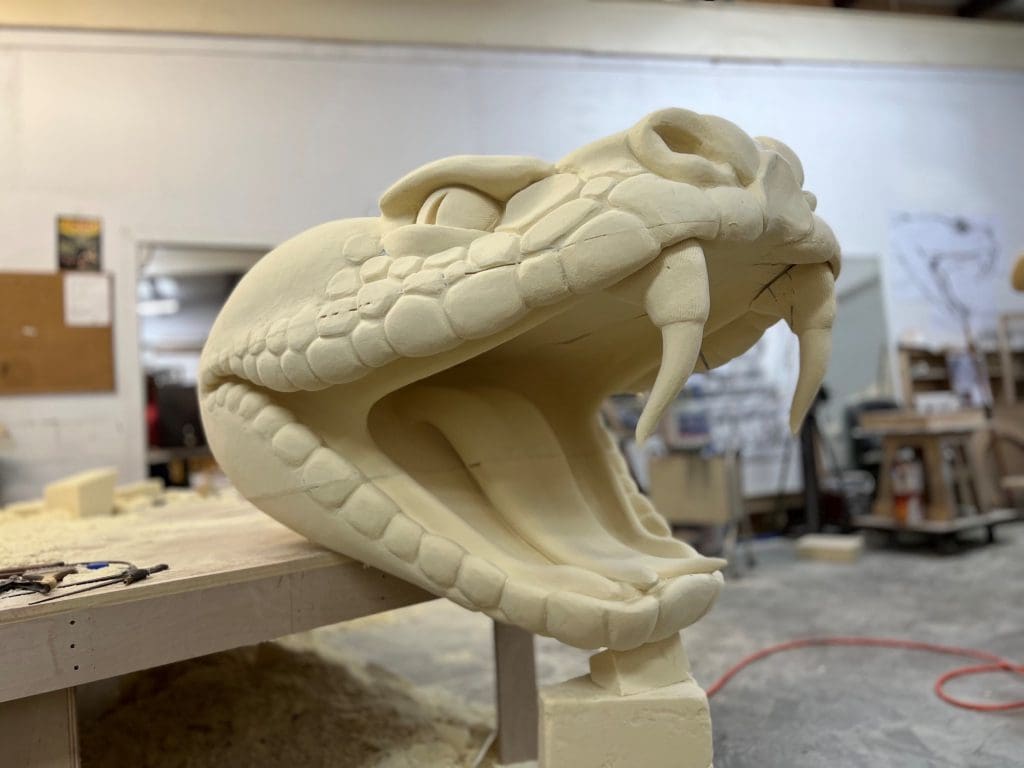a close up of a large unpainted sculpture of a snake head with large fangs