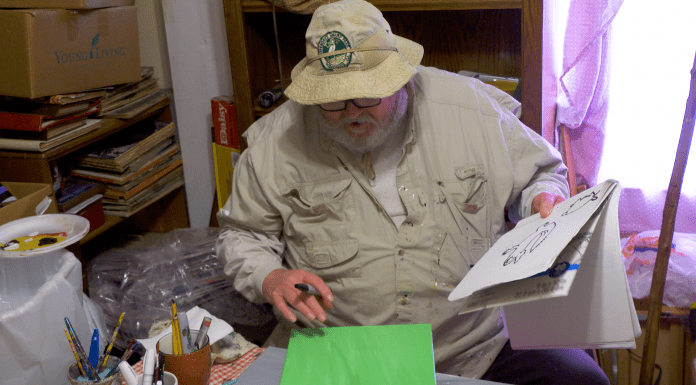 Valdosta Man Battles Glaucoma With A Paintbrush and a Positive Attitude A person sitting at a table wearing a hat