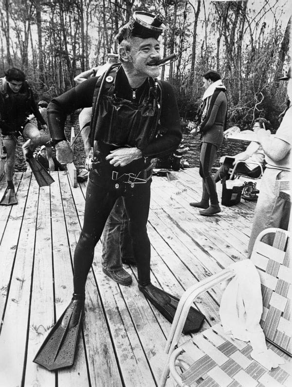 Jack Lemmon in scuba suit and cigar on wooden dock.