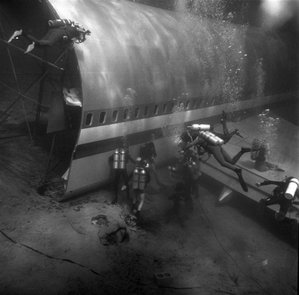 A group of people in scuba gear around one-half of an underwater plane.