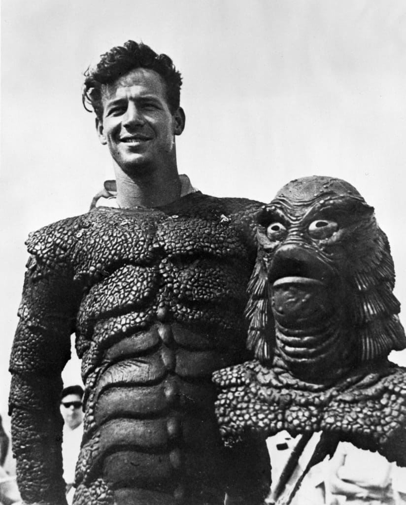 Ricou Browning posing for the camera in Creature of Black Lagoon costume.  He is holding the creature's head.