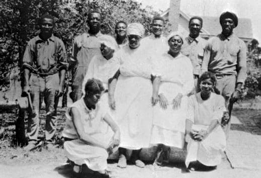 A  group of men and women posing for camera.   Six men in the back and 5 women wearing white in the front.