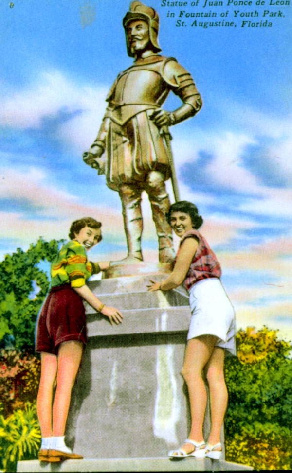 Two women  posing for the camera in front of a statue dressed in armor.  i upper right hand corner it says 
