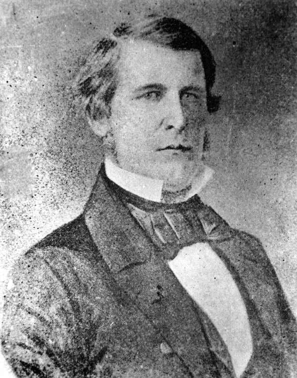 A faded black and white photograph of a man with a serious expression wearing a high color, a suit and a tie. 