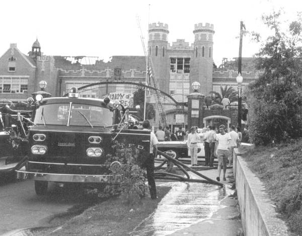 A firetruck, hoses, and drowd of people in front of the Westcott building on FSU's campus.  the turrets and the north side of the building can be seen as well as a hole in the roof from a fire.