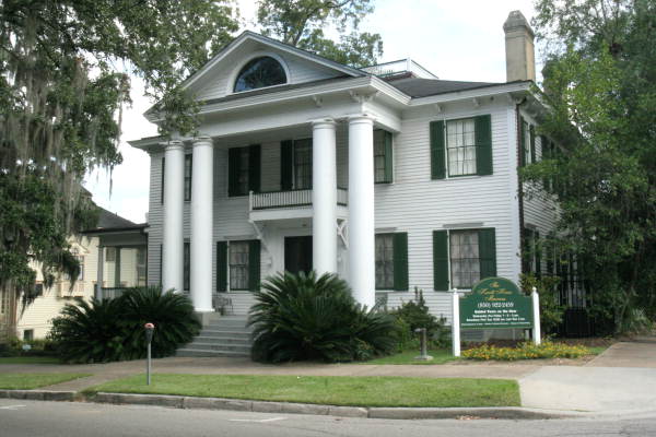 A two story white house with dark shutters, columns and a chimney.
