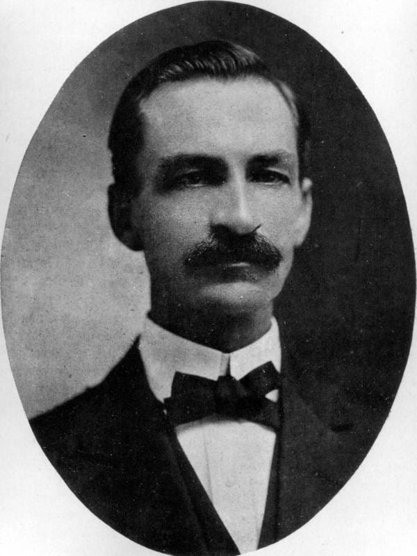 A vintage photo of a man with mustache wearing a suit and bow tie