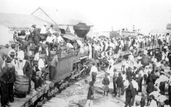 A large group of people standing and climbing on  a train while another group stands next to it.