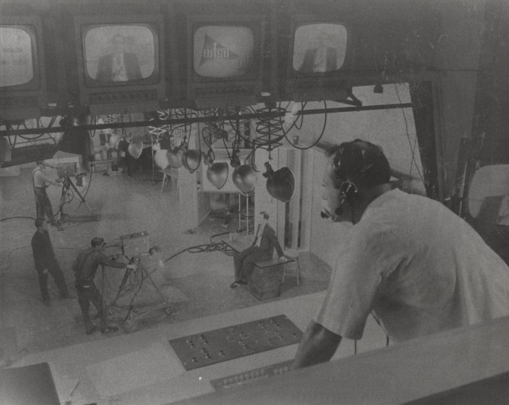 black and white photo of man looking out window to studio below.