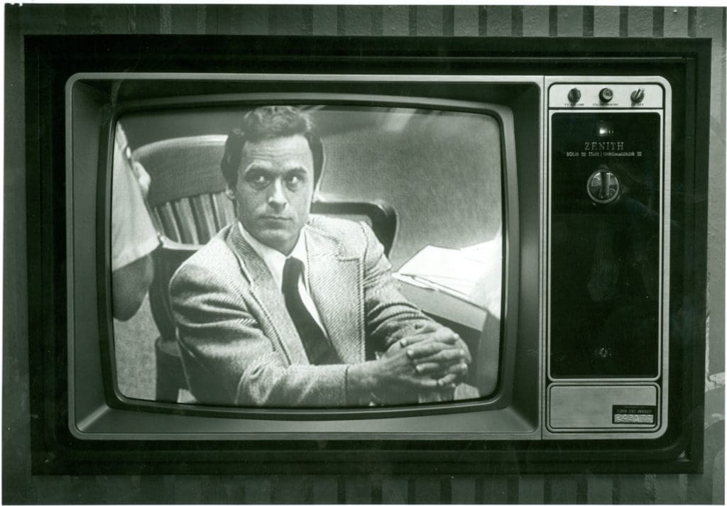 TV set showing Ted Bundy sitting in court in suit and tie.
