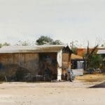 A truck driving down a dirt road in front of a building