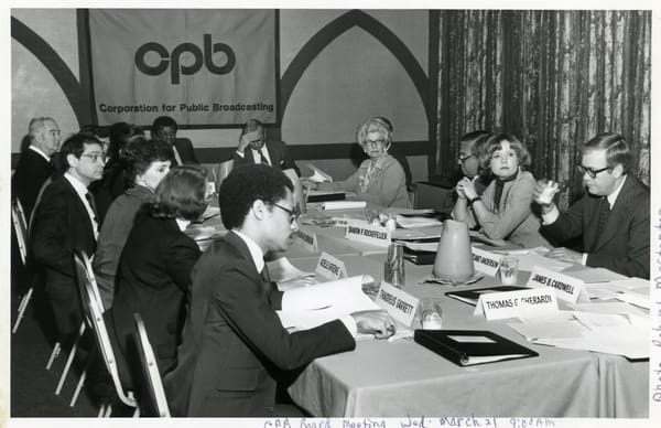 A group of people sitting at a table. In the background is a CPB banner.