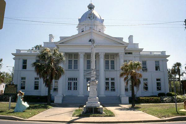 A statue and palm trees in front of a courthouse.