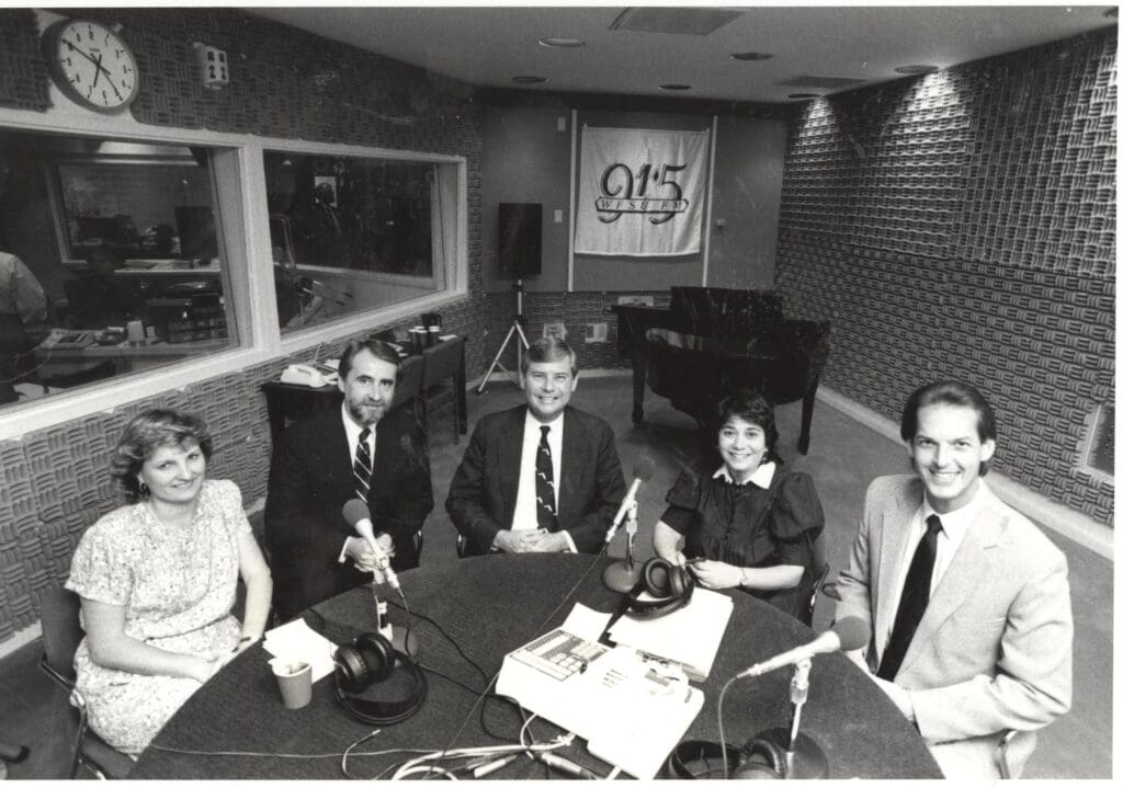 Bob Graham and four other people sitting at at a round table with piano in background 
