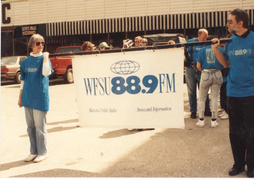 Two people wearing WFSU 88.9 shirts holding a banner that says WFSU 88.9 FM.