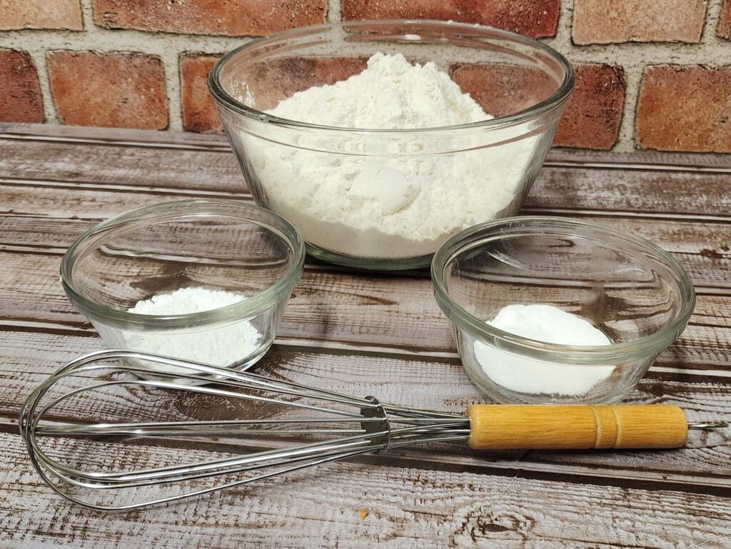 side shot of three bowls  with white ingredients and a whisk.