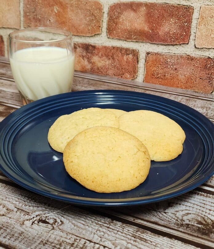three cookies on a blue plate next to a glass of milk