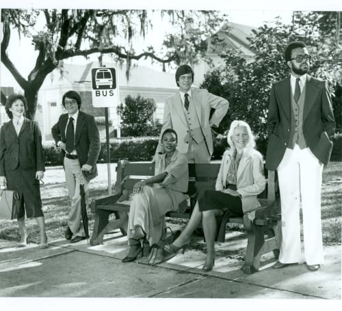 A group of people standing around a bench as though they are waiting for a bus