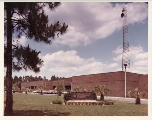 A large brick building with grass and trees. WFSU Tower is seen in the background 