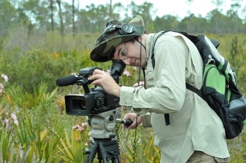 A person standing next to a video camera in a field