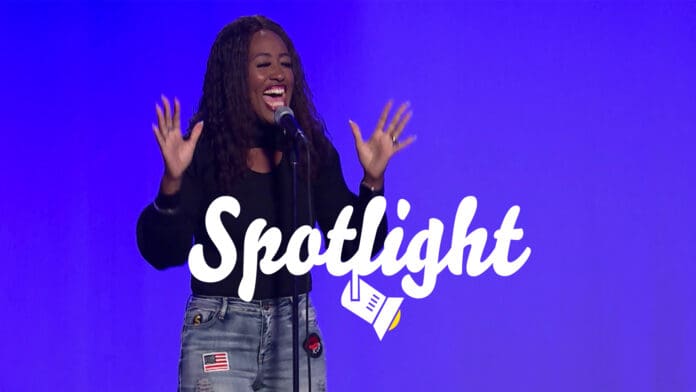 Woman singing in front of blue background.