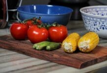 Chef Fe’s Okra & Tomato Stew Two tomatoes sitting on top of a wooden cutting board with okra and corn cobs
