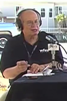 panel of guests sitting at a table outdoors with microphones and headphones