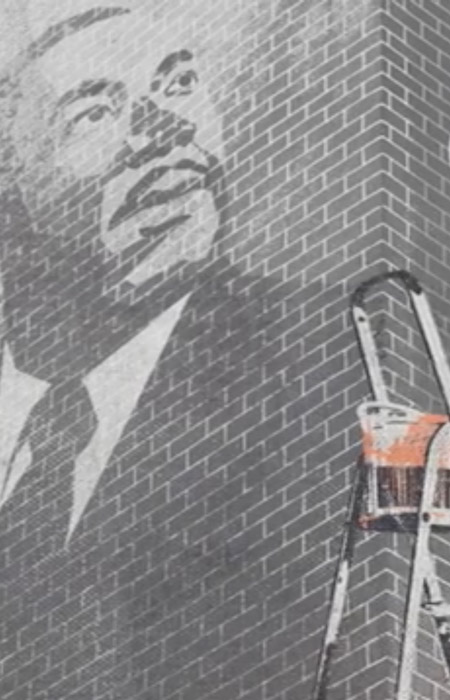 black man in suit and tie superimposed on a brick wall next to paint can on ladder