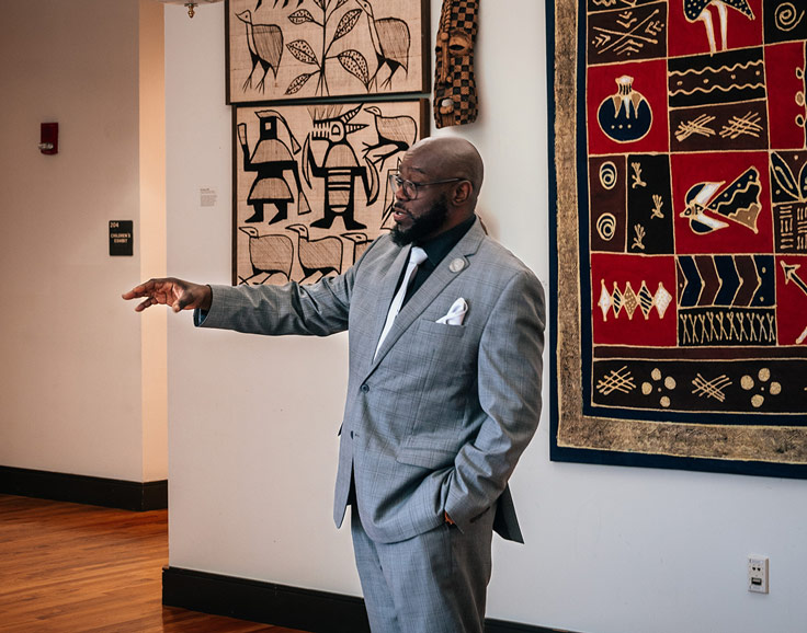 a man in a suit describing African American art displayed behind him inside a museum