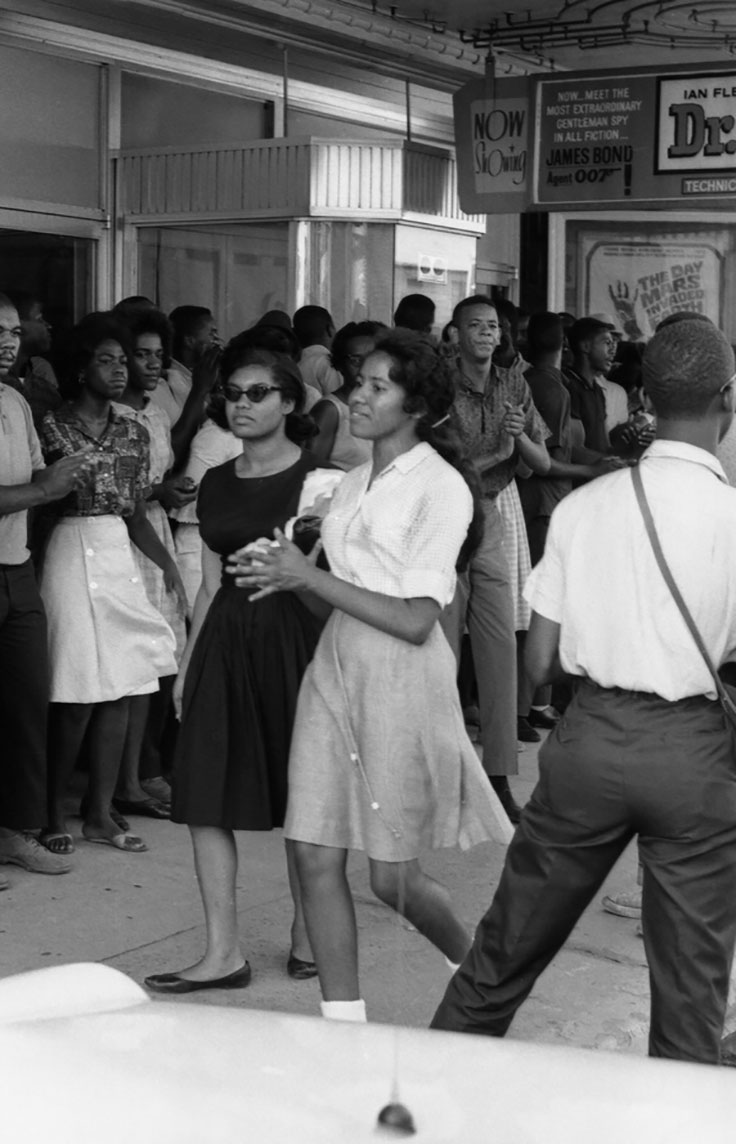 two women, circa 1960s, walking in a crowd on the downtown sidewalk, one is wearing sunglasses