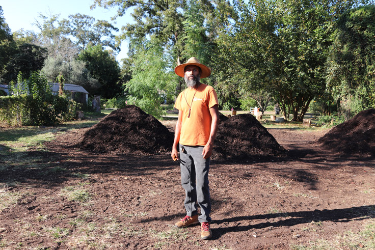 a man standing in front of large compost piles