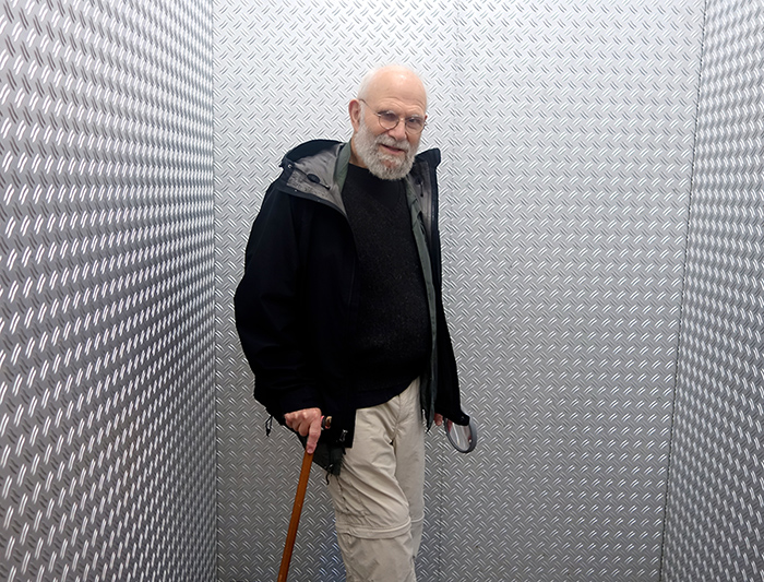 older man standing with cane in small room with metal walls, black and white photo