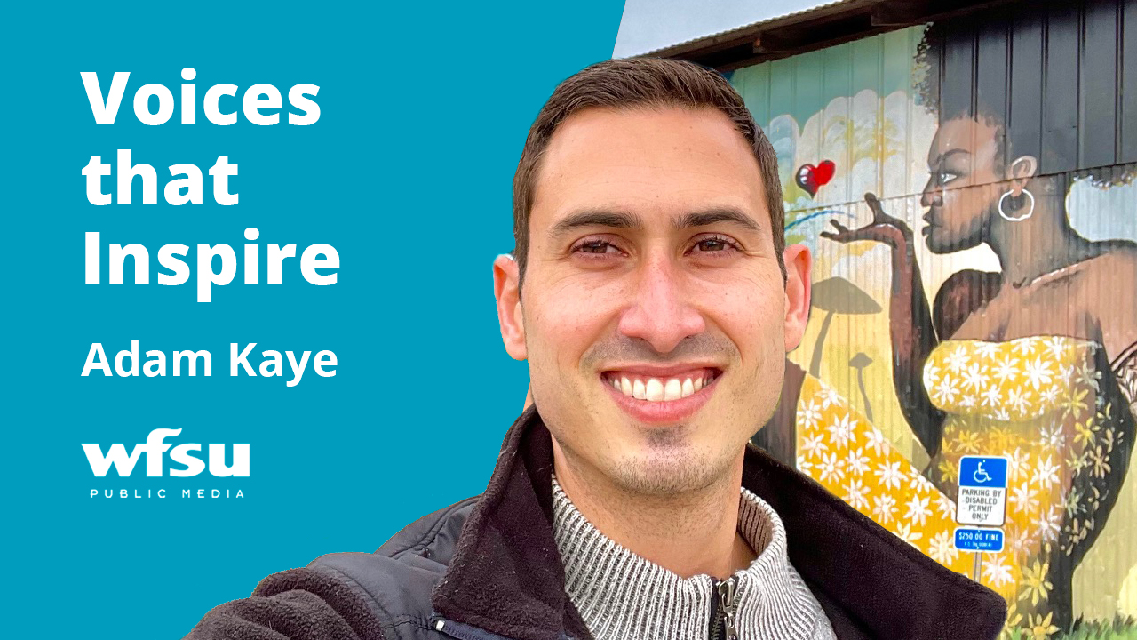 Man smiling in front of a mural painted on a wall.