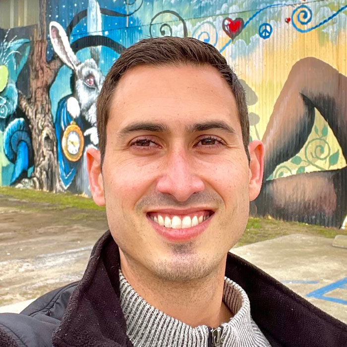 Man smiling in front of a mural painted on a wall.