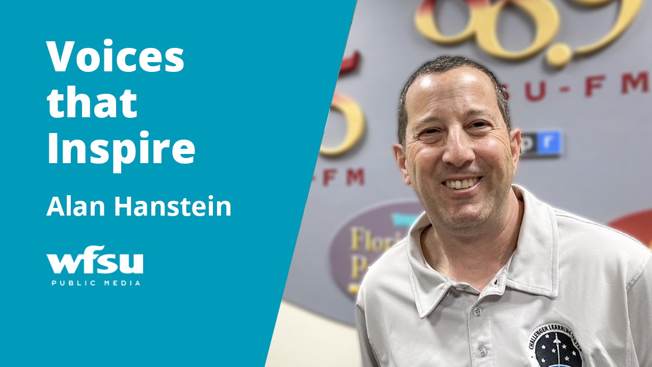 A smiling man stands in front of a  grey background with garnet and gold letters and numbers.