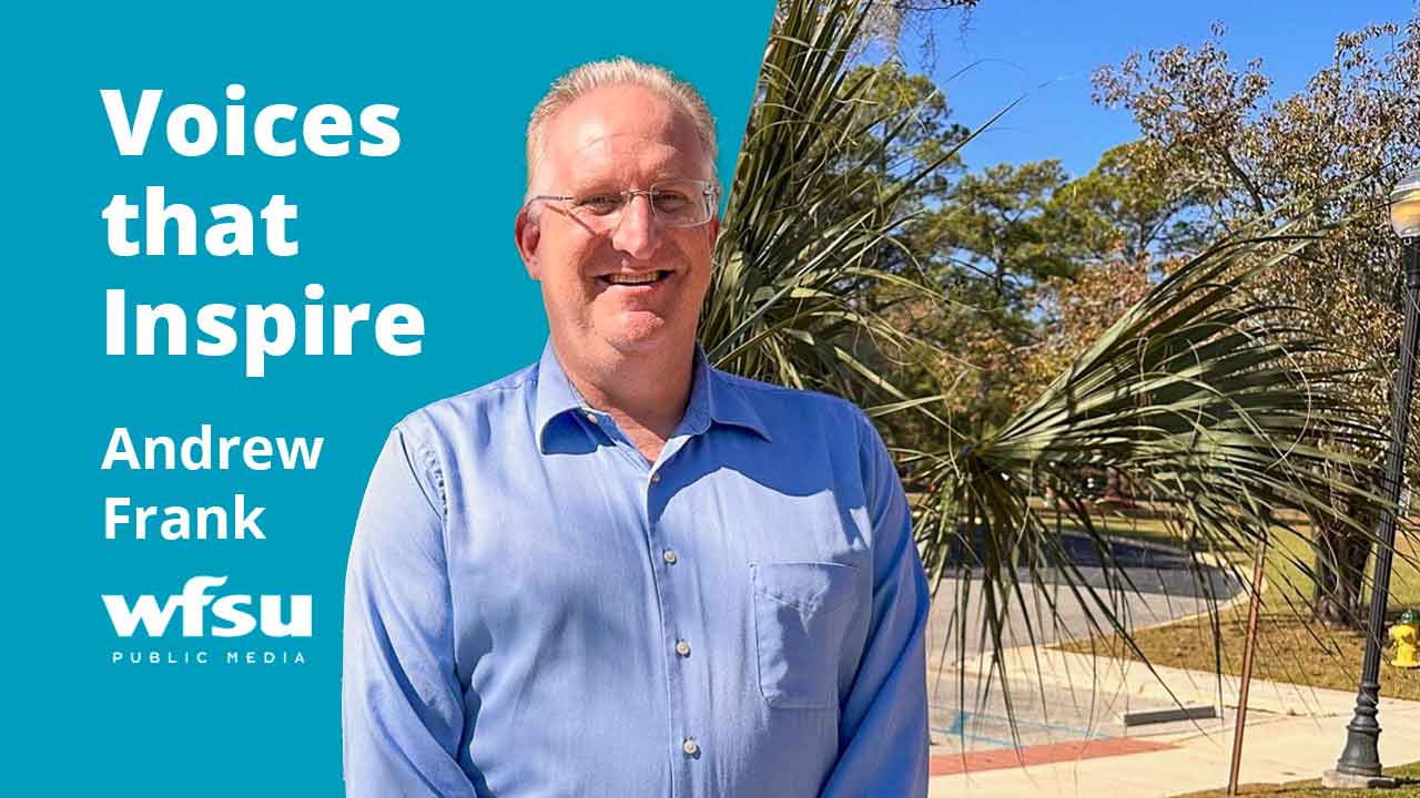 A smiling man stands in front of a bush.
