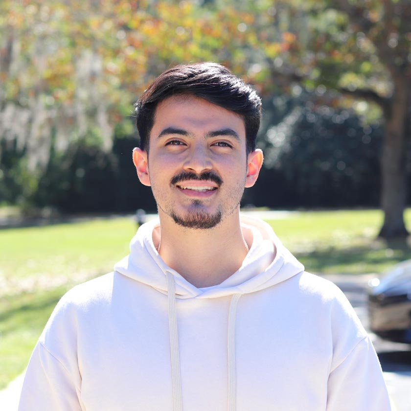 A man in a white hoodie stands smiling outside.