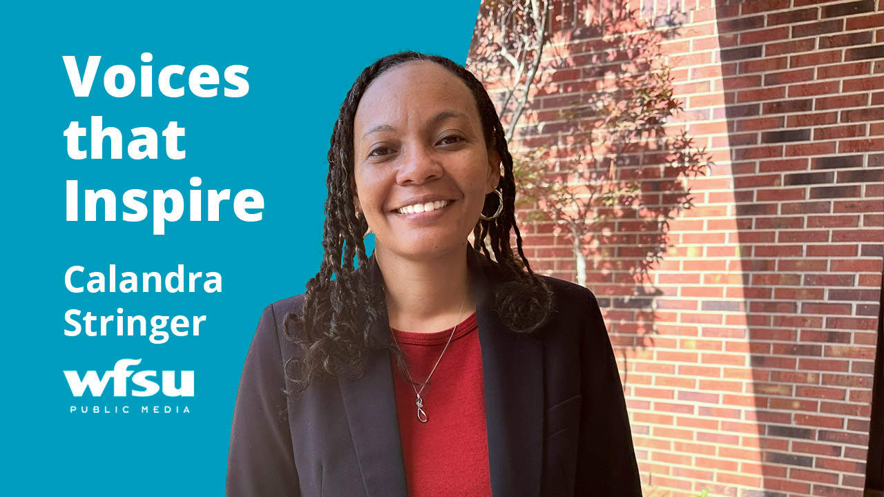 A smiling woman stands outside in front of a red brick wall.