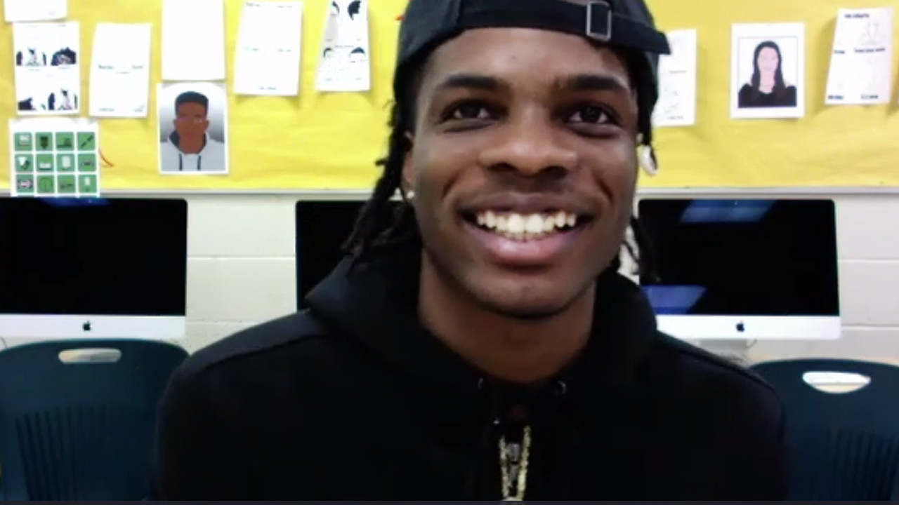 young man in a cap smiling, sitting in classroom