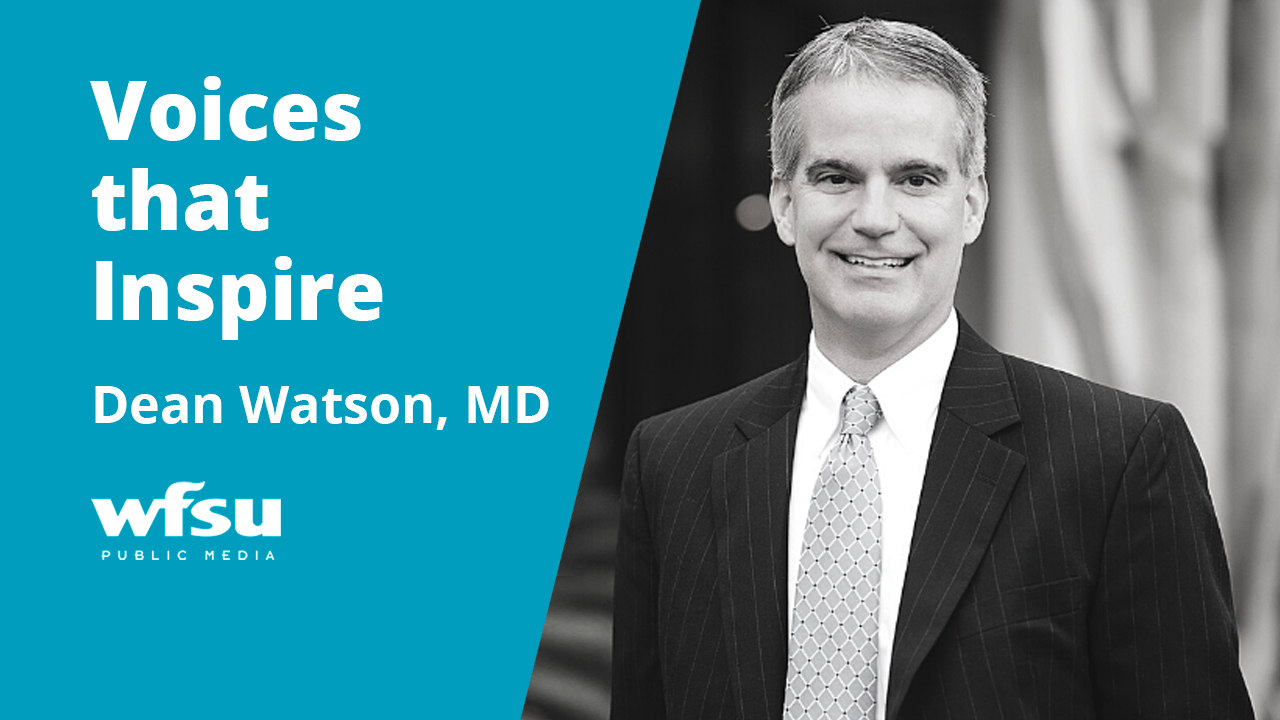 A man smiling in a dark suit and tie.