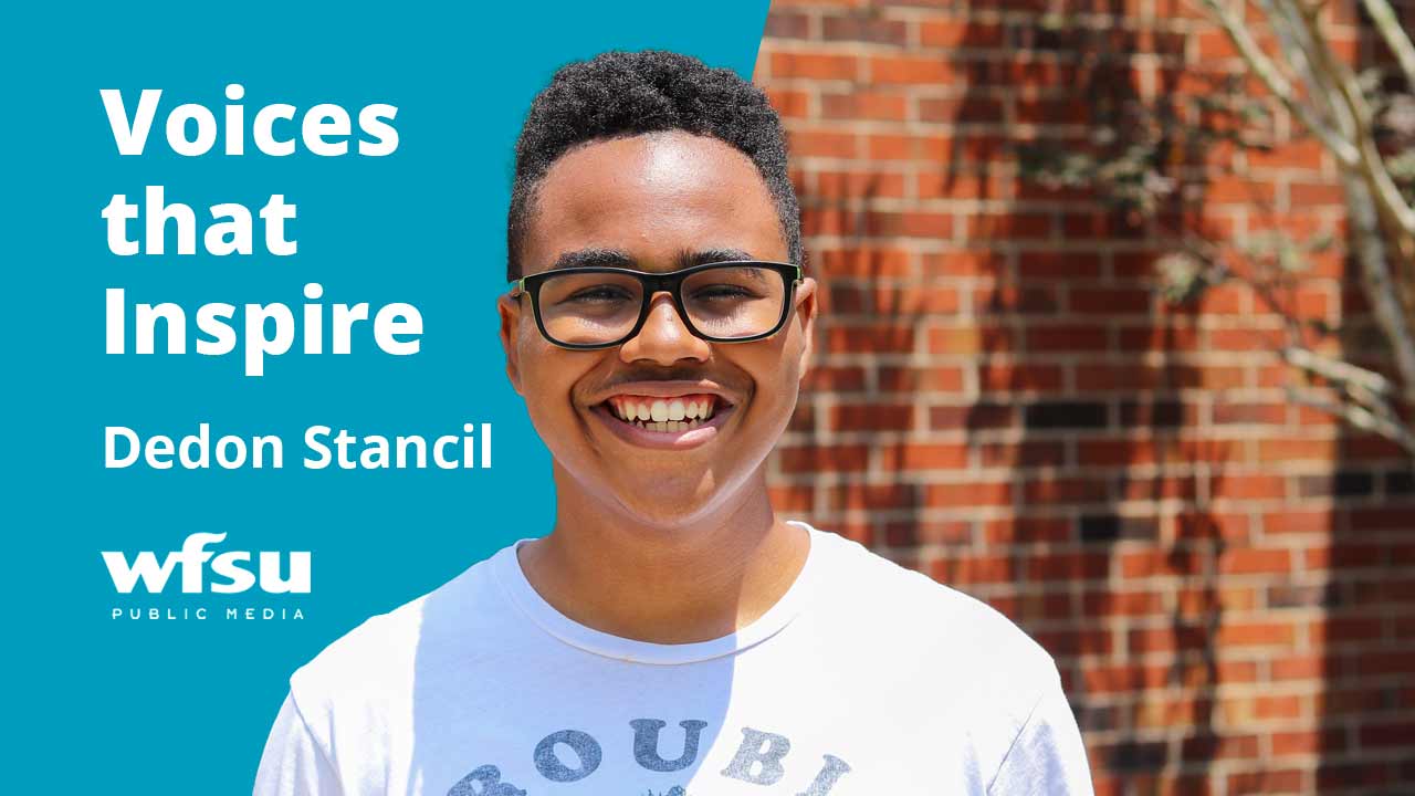 A smiling man stands in front of a red brick wall.