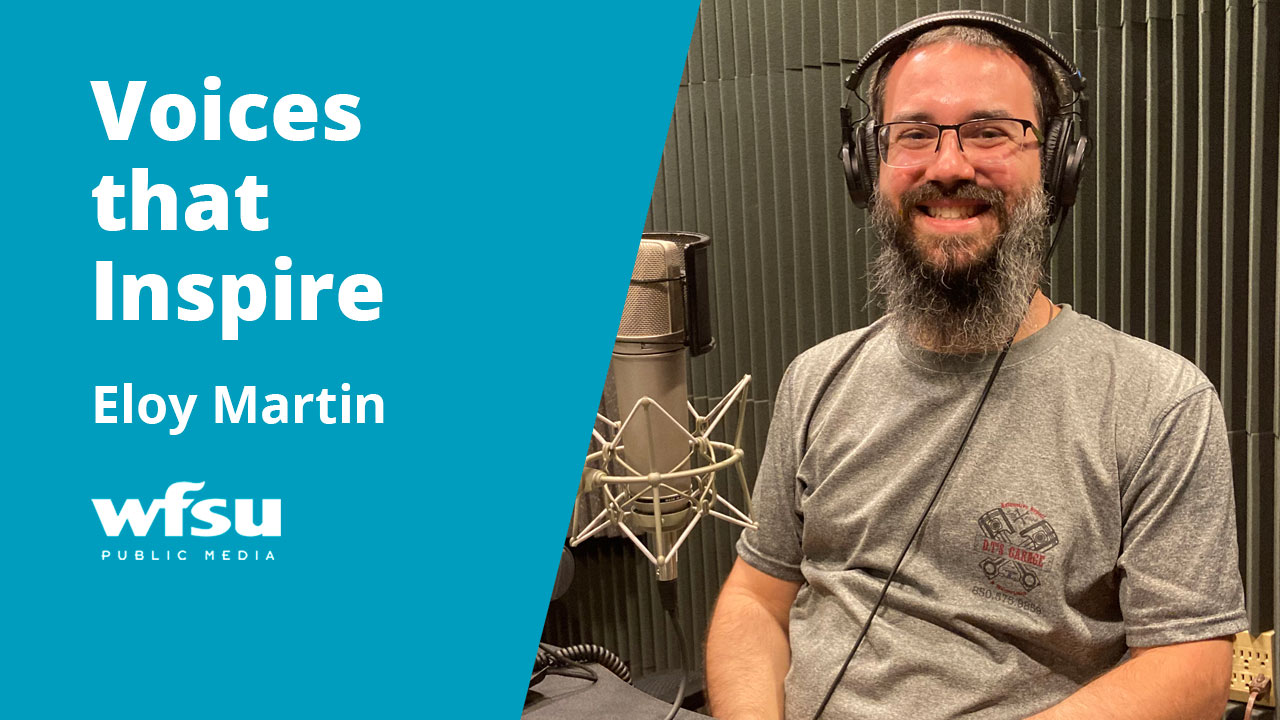 A man with a large beard is smiling and wearing headphones.