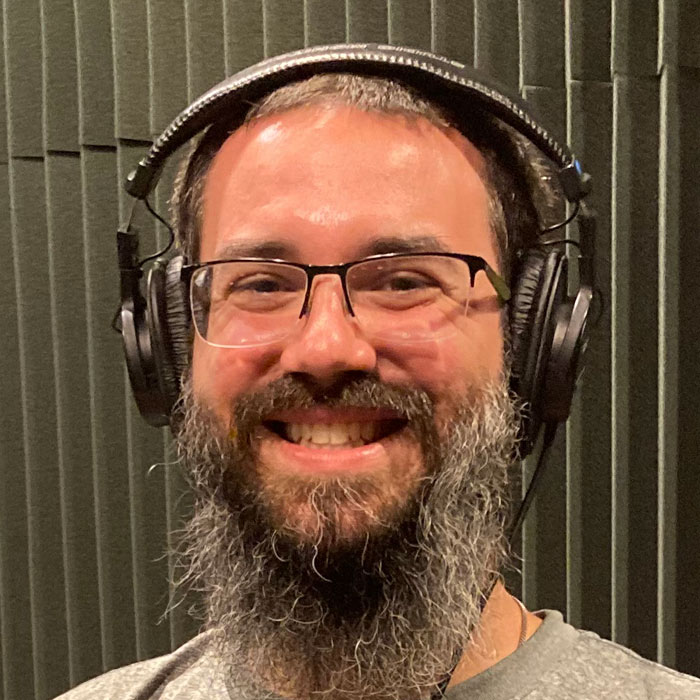 A man with a large beard is smiling and wearing headphones.