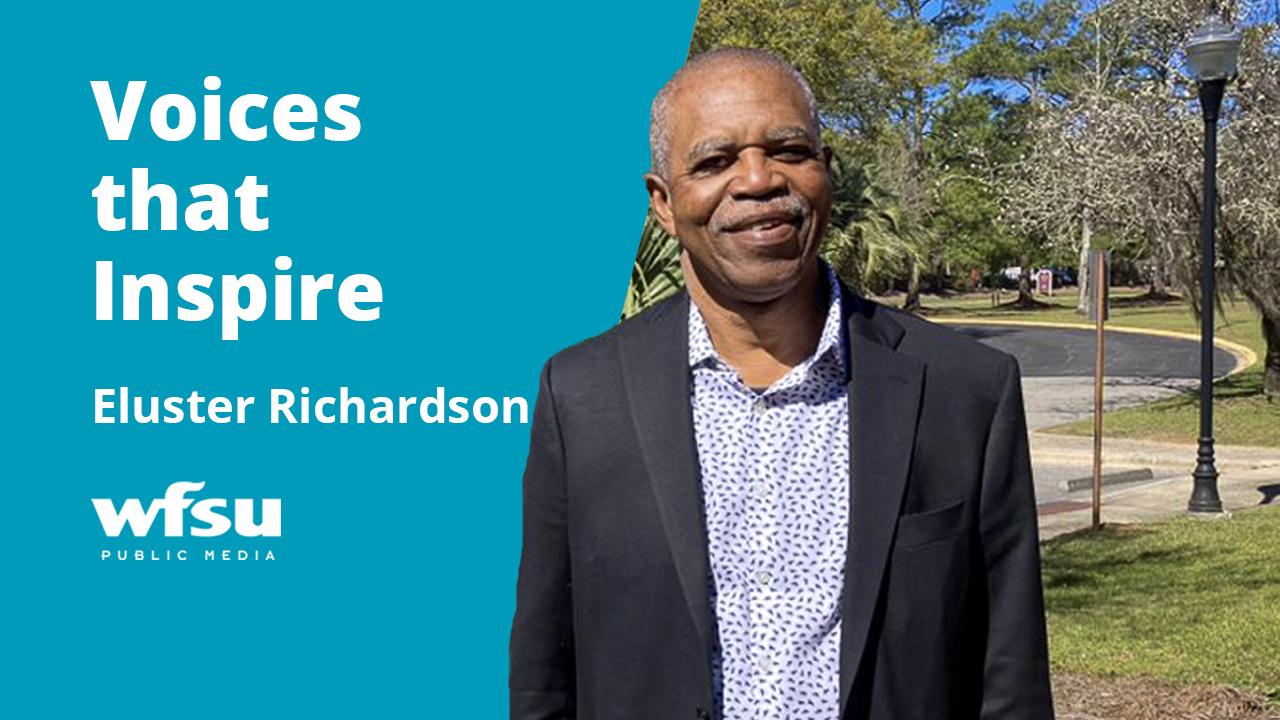 A smiling man in a dark suit stands outside.
