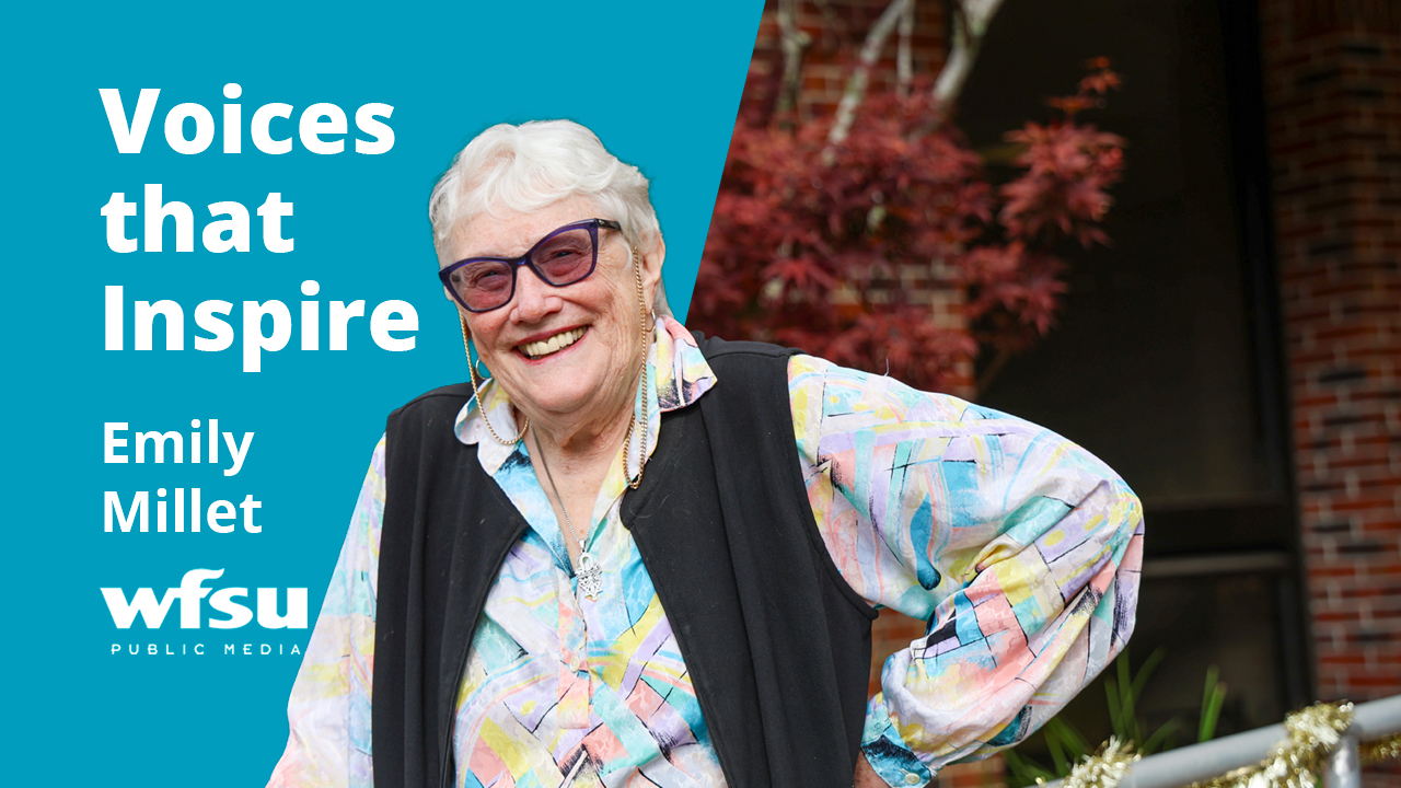 A smiling woman stands in front of a red-brick wall