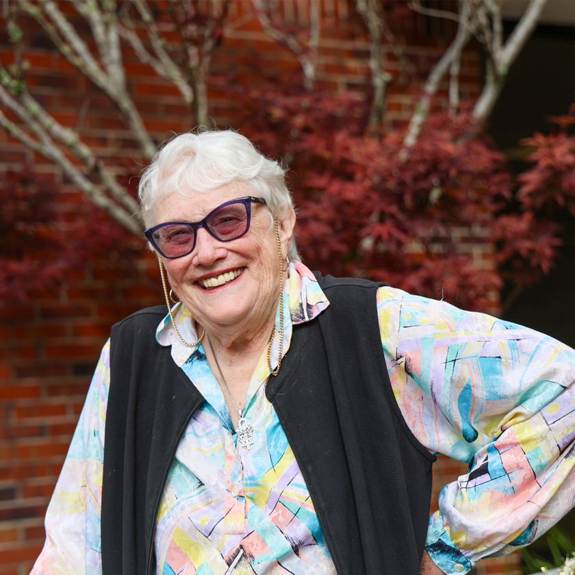 A smiling woman stands in front of a red-brick wall