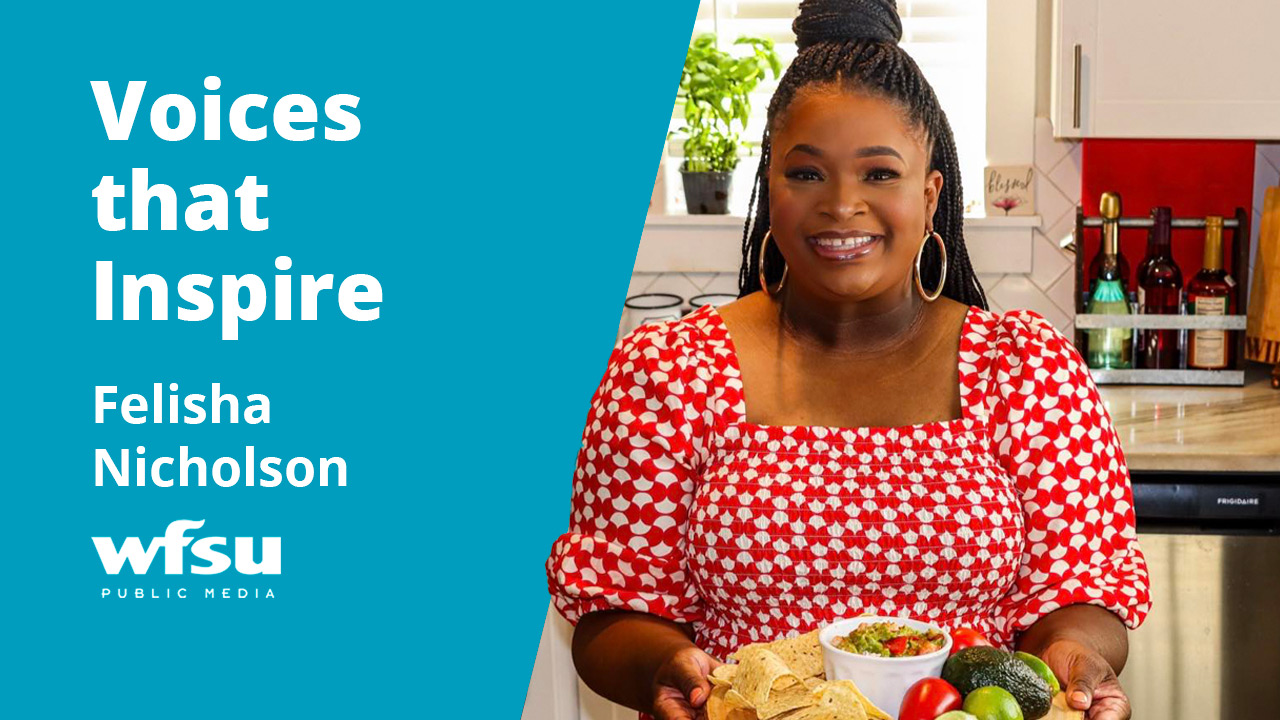 A smiling woman dressed in red and white stands in a kitchen holding a plate of food.