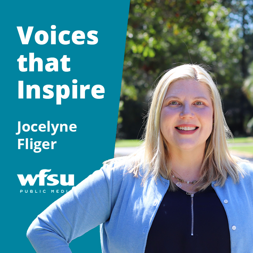 A smiling woman stands otside in front of a tree.