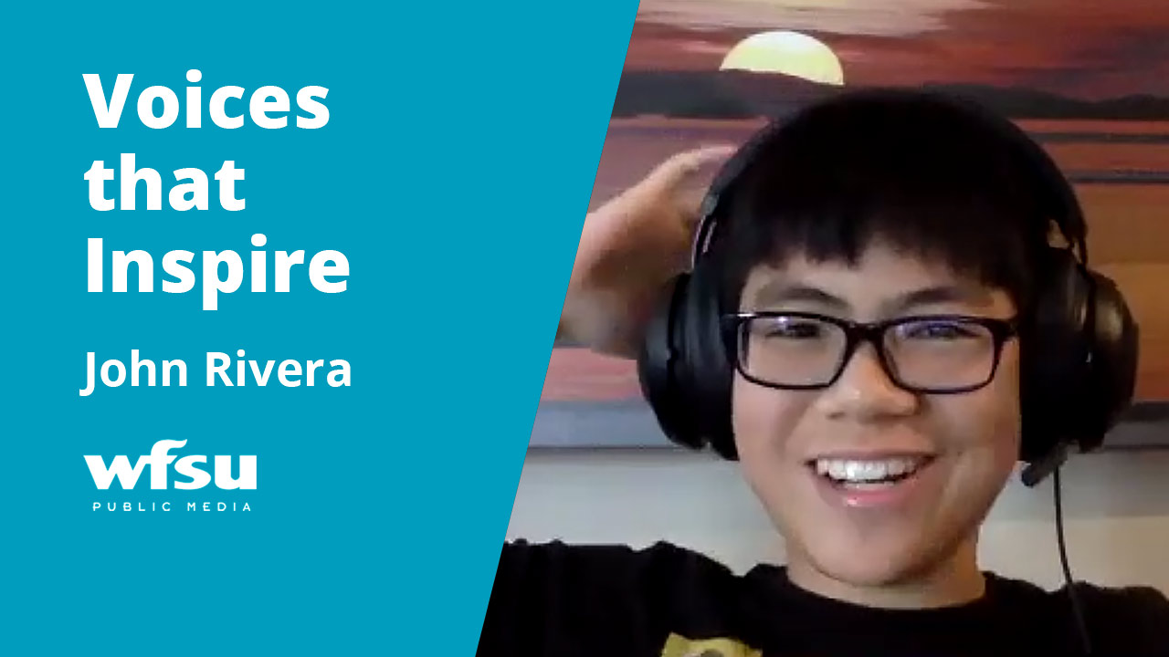 A young man in a black t-shirt wearing large over-the-ear headphones and glasses is smiling.